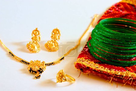 Concept , gold and black beads necklace mangalsutra green glass bangles earrings with wedding ring and sari imitation jewellery on white background