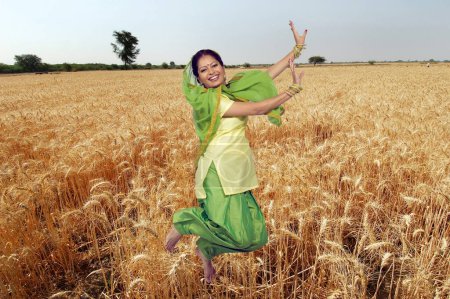 Foto de Mujer sij realizando danza folclórica bhangra en campo de trigo - Imagen libre de derechos