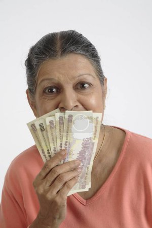 Anciana sosteniendo en una mano cinco notas de 500 rupias cada una y manteniéndolas muy cerca de la cara 