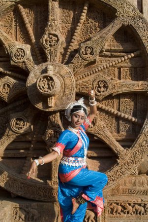Téléchargez les photos : La pose de la danseuse Odissi reproduit des mythes indiens tels que le Ramayana devant l'emblématique Sun Chariot dans le complexe du temple solaire du patrimoine mondial à Konarak, Orissa, Inde - en image libre de droit
