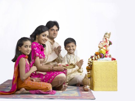 Photo for South Asian Indian family with father mother son and daughter sitting praying to lord Ganesha - Royalty Free Image