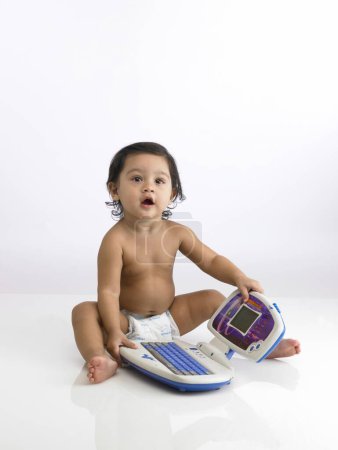 Indian baby girl wearing diaper playing with toy laptop