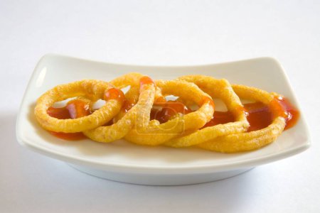 Téléchargez les photos : Cuisine indienne, entrées fast-food Kandy Bhaji beignets d'oignons croustillants anneaux servis avec ketchup tomate dans un plat sur fond blanc - en image libre de droit