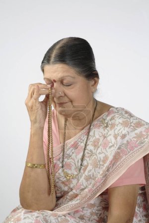 Alte Dame betet mit Rosenkranz oder Japmala in der rechten Hand, die das rechte Auge berührt