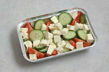 Téléchargez les photos : Salade, tranches de concombre, tomates, salade Iceberg hachées et fromage conservé dans un récipient en aluminium à emporter - en image libre de droit