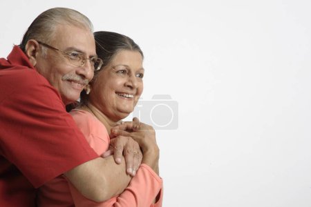 Altes Paar, alter Mann hält alte Frau neben sich und lächelt 