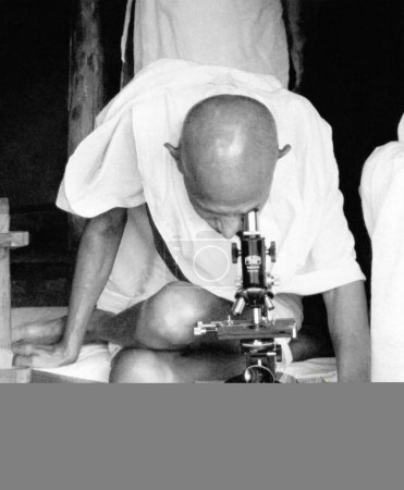 Téléchargez les photos : Mahatma Gandhi et l'assistant de l'hôpital Shankaranji au microscope observant des germes de lèpre à l'ashram de Sevagram, vers 1942 - en image libre de droit