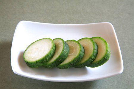 Téléchargez les photos : Légume vert, tranches rondes de ghiya nanuan rampant pompion sorte de citrouille dans une plaque rectangle sur fond gris - en image libre de droit