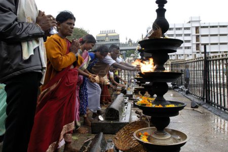 Photo for Devotees worshipping and offering coconut; camphor and flowers to Lord Venkateshwara (Balaji) in front of the huge oil lamps  at Tirumala temple; Tirupati ; Andhra Pradesh ; India - Royalty Free Image