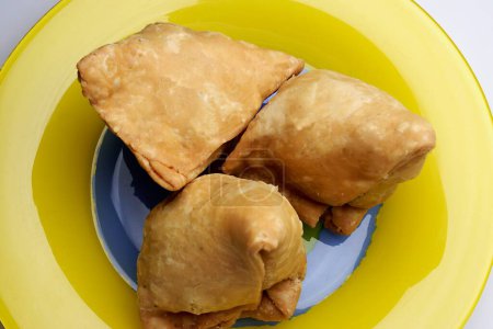 Téléchargez les photos : Collation indienne nourriture frite samosa pomme de terre remplissage trois morceaux dans une assiette jaune - en image libre de droit