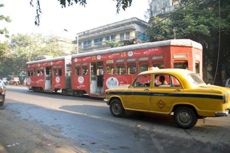 Téléchargez les photos : Tram ancienne façon de service de navette avec taxi de couleur jaune sur la route ; Calcutta maintenant Kolkata ; Bengale occidental ; Inde - en image libre de droit
