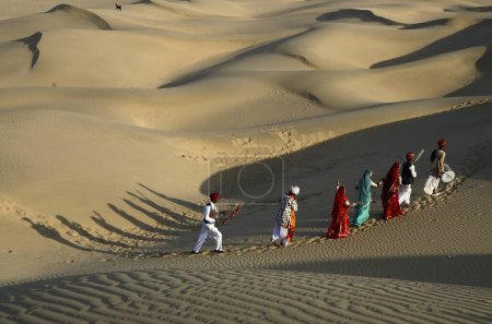 Téléchargez les photos : Musicien folklorique et danseurs marchant sur une dune de sable à Jaisalmer au Rajasthan Inde - en image libre de droit