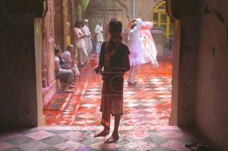 Photo for Silhouette of child smeared in colored powder and devotees dancing, singing, rejoicing and playing Holi at Radha Vallabh temple, Vrindavan, Uttar Pradesh, India - Royalty Free Image