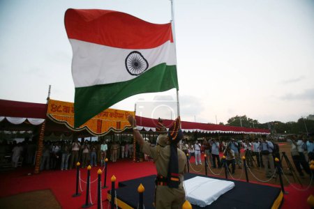 Téléchargez les photos : Homme de police apportant le drapeau national indien vers le bas pendant le coucher du soleil le 1er mai Maharashtra jour de la fondation de l'État, parc Shivaji, Dadar, Bombay Mumbai, Maharashtra, Inde - en image libre de droit
