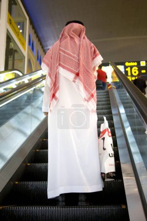 Foto de Hombre en árabe blanco tradicional vestido en escalera automática, Aeropuerto Internacional de Dubai, Dubai Oriente Medio Emiratos Árabes Unidos - Imagen libre de derechos