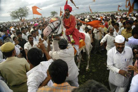 Foto de Caballo portador de la bandera santa rodeado de devotos en ringan yatra en la feria anual de Pandharpur, Pandharpur, Maharashtra, India - Imagen libre de derechos