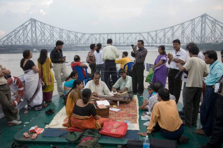 Photo for Musician performing on boat in river hooghly ; Howrah bridge now Rabindra Setu steel structure amazing feat of engineering ; Calcutta now Kolkata ; West Bengal ; India - Royalty Free Image