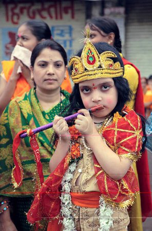 Téléchargez les photos : Janmashtami festival ou fête d'anniversaire du Seigneur Krishna carnaval Enfant déguisé en Seigneur Krishna jouer de la flûte avec la mère en arrière-plan aussi rejoindre, Jabalpur, Madhya Pradesh, Inde - en image libre de droit