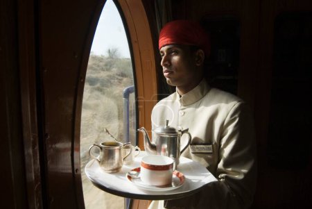 Téléchargez les photos : Rajasthani préposé tenant plateau de boisson dans Heritage on Wheels Voyage dans le train touristique de luxe passé ; Rajasthan ; Inde - en image libre de droit