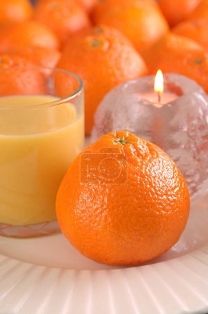 Foto de Fruta, naranja (Citrus reticulata, Clcement, Rutaceae) Zumo de naranja en vidrio y vela ardiendo en candelabro de cristal en forma de naranja - Imagen libre de derechos