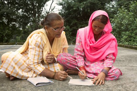 Foto de Voluntariado enseñando a anciana a escribir programa de alfabetización de adultos iniciativa socioeconómica iniciada por la ONG Chinmaya Organización de Desarrollo Rural CORD, Sidhbari, Himachal Pradesh, India - Imagen libre de derechos