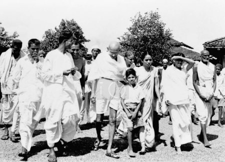 Foto de Mahatma Gandhi, acompañada por la periodista Shailendra Chatterjee 4ta de l, Abha Gandhis hermana Vinabehn Patel 3ra r de Mahatma Gandhi y otros caminando en Sevagram Ashram, 1944 - Imagen libre de derechos
