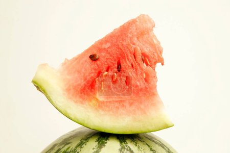 Fruits ; Watermelon cut into quarter piece showing red watery pulp with black seeds placed above one full melon ; Pune ; Maharashtra ; India