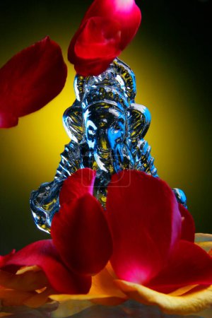 Foto de Mesa Estudio plano de ídolo de vidrio del Señor Ganesh Ganapati, Elefante encabezó a Dios con pétalos de rosa de color amarillo - Imagen libre de derechos