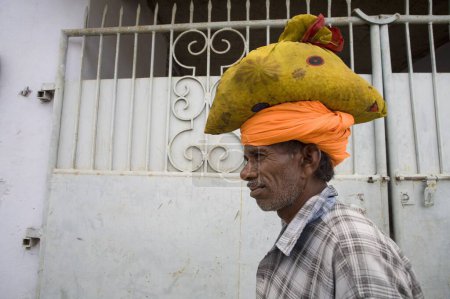 Photo for Indian rural old man wearing orange turban and carrying heavy load on head Village Dilwara, Udaipur, Rajasthan, India - Royalty Free Image