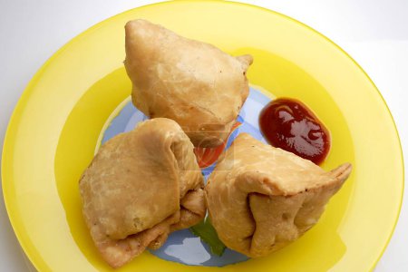 Téléchargez les photos : Collation indienne nourriture frite samosa pomme de terre remplissage de trois morceaux dans une assiette jaune avec ketchup - en image libre de droit