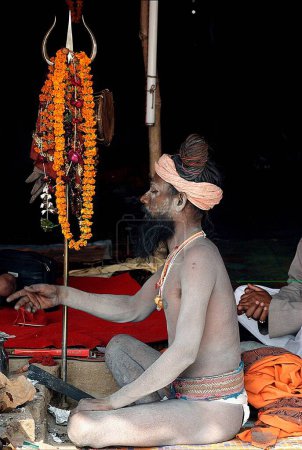 Téléchargez les photos : Un naga sadhu de la Juna Akadha est assis avec son Trishul au camp pendant l'Ardh Kumbh Mela, en Inde - en image libre de droit