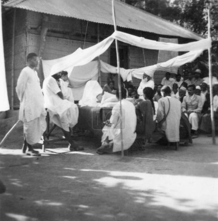 Téléchargez les photos : Mahatma Gandhi parler les gens tout en prenant un bain de soleil village Dasgharia Noakhali Est Bengale Kanu Gandhi est resté Novembre 1946 - en image libre de droit
