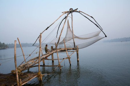 Foto de Pescador parado en la plataforma de la red china observando aguas tranquilas cerca de la isla Bolgatty, Ernakulam, Kerala, India - Imagen libre de derechos