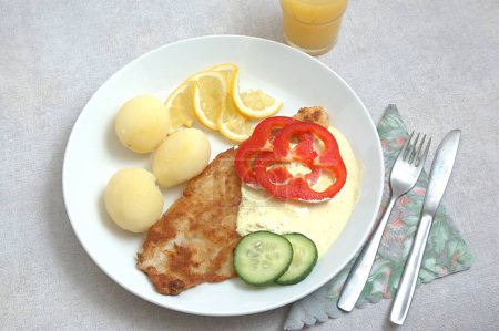 Food , Fried fish (Pangausuise filed Vietnamese fish farmed in rice fields ) with Danish remold sauce and cooked potatoes garnished with cucumber and red bell peppers and slices of lemon , knife , fork and glass of juice