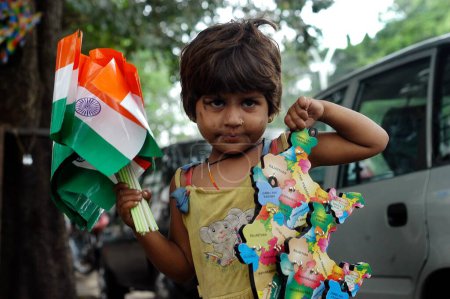 Photo for Small girl child laborer selling Indian flags and plastic mould Indian maps on roads in Bombay now Mumbai ; Maharashtra ; India - Royalty Free Image