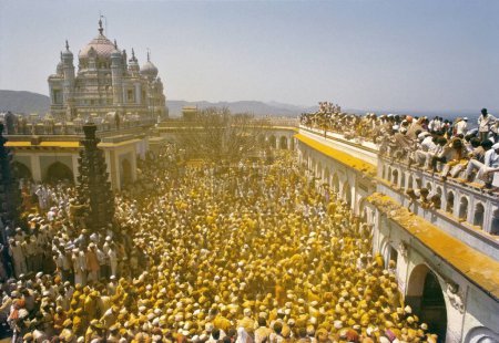 Téléchargez les photos : Le palanquin portant les images de Khandoba et Malshabai quitte la porte du temple, la foule explose en slogans rituels, couvrant tout le monde dans la parenté jaune de dévotion, Jejuri, Maharashtra, Inde - en image libre de droit