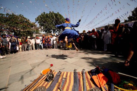 Téléchargez les photos : Guerrier nihang ou sikh effectuant des cascades avec épée et bouclier lors des célébrations Hola Mohalla à Anandpur sahib dans le district de Rupnagar, Punjab, Inde - en image libre de droit