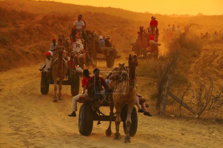 Photo for People travelling in camel cart at sunset for Pushkar fair ; Rajasthan ; India - Royalty Free Image