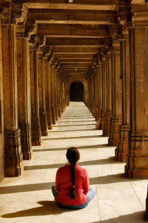 Téléchargez les photos : Femme en pull rouge assise dans la posture méditante dans le passage de Jumma masjid ; Ahmedabad ; Gujarat ; Inde - en image libre de droit