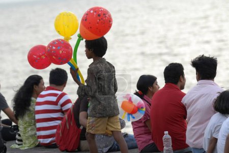 Téléchargez les photos : Un jeune garçon vend des ballons colorés à des touristes visitant Marine Drive à Bombay Mumbai, Maharashtra, Inde - en image libre de droit