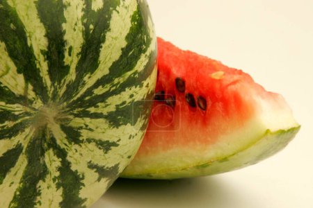 Fruits ; One full watermelon with light and dark green stripes and one cut slice showing red watery pulp with black seeds  ; Pune ;  Maharashtra ; India