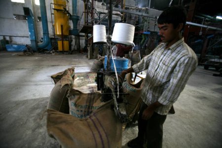 Téléchargez les photos : Un travailleur scellant l'embouchure du sac de jute contenant du sucre à l'usine de sucre de Sangli ; Maharashtra ; Inde - en image libre de droit