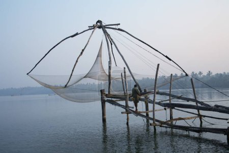 Foto de Pescador parado en plataforma de red china observando aguas tranquilas cerca de la isla Bolgatty Temprano en la mañana Ernakulam; Kerala; India - Imagen libre de derechos