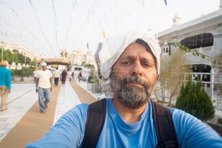 Téléchargez les photos : Barbe homme tête couverte de tissu blanc marchant Swarn Mandir Golden temple, Amritsar, Punjab, Inde - en image libre de droit