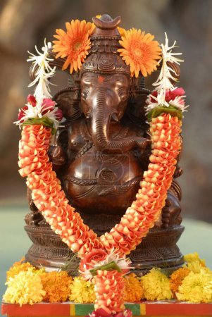Idol ricamente tallado en madera del Señor Ganesh pintado como metal de cobre; guirnaldas por coloridas flores artificiales y caléndula; elefante con cabeza de Dios Ganapati; Bombay Mumbai; Maharashtra; India