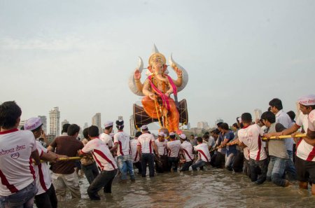 Téléchargez les photos : Volontaires traînant énorme idole de Ganpati pour l'immersion en mer à Girgaon Chowpatty Mumbai Inde Asie - en image libre de droit