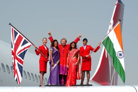 Téléchargez les photos : Propriétaire de Virgin Atlantic Airways Richard Branson ainsi que des modèles indiens et hôtesse de l'air tenant le drapeau de l'Inde et de la Grande-Bretagne sur les ailes d'Airbus A340 600 - en image libre de droit