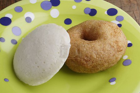 Indian fried snack medu wada and steamed idli on yellow plate