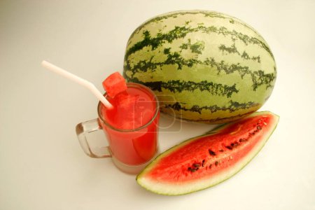 Fruits ; One full watermelon with light and dark green stripes with glass of melon juice and cut slice showing red watery pulp and black seeds ; Pune; Maharashtra ; India