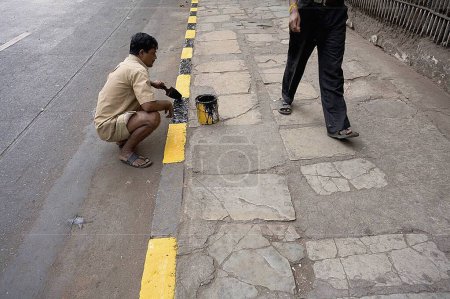 Foto de Hombre pintando pavimento bordillo de piedra en negro y amarillo, Bombay Mumbai, Maharashtra, India - Imagen libre de derechos